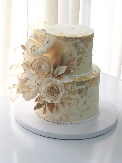 Handcrafted sugar roses, delicate gold leaf, and a love story ready to unfold. This ivory and gold two-tiered wedding cake is a symbol of forever.