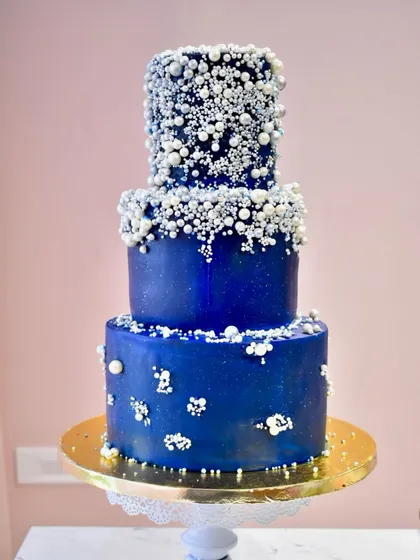 A grand three-tier Sangeet cake designed to sparkle under the lights. The deep blue fondant is decorated with a cascade of edible silver and white pearls, creating a galaxy-like effect perfect for a night of celebration.