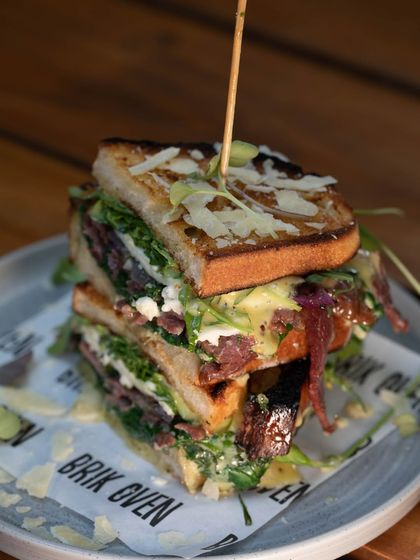 Our fully loaded ciabatta sandwich, stacked three layers high and held together with a skewer. It's packed with cured meats, cheese, and arugula.