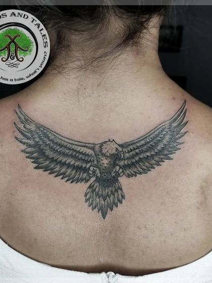 A powerful eagle with its wings spread wide, tattooed across the upper back. The black and grey shading gives the feathers a realistic texture and sense of movement.