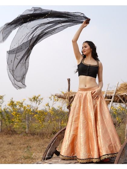 A beautiful peach brocade lehenga paired with a simple black sleeveless blouse and a flowing black organza dupatta. The contrast is modern and striking.
