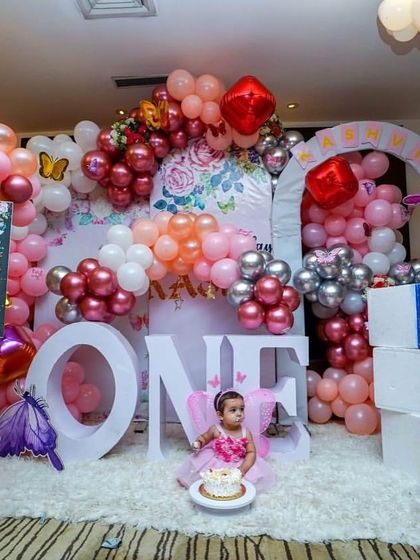 A beautiful butterfly-themed first birthday with the birthday girl right in the middle of the decor. The setup includes a milestone board, 'ONE' blocks, and a mix of pink, white, and silver balloons.