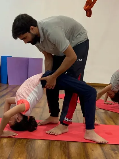 An instructor provides a gentle adjustment to a child in a wheel pose, ensuring safe practice and proper alignment.