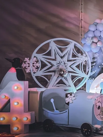 A detailed shot from the winter wonderland party, showing a custom-made snowflake ferris wheel and a penguin prop next to a light-up number '4'.