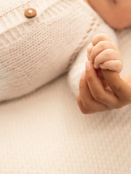 A tiny hand holding tight to a parent's finger. This close-up shot shows the delicate details of their little fingers and the strength of their grip.