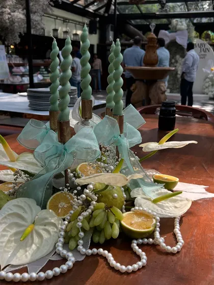 An elegant centerpiece featuring twisted mint-green candles, white anthuriums, fresh grapes, and pearls, tying the whole decor theme together.