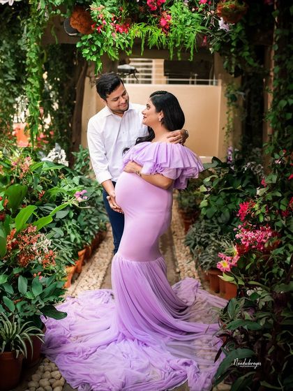A fairytale moment in a lush garden path. The couple is framed by greenery, with the mother-to-be's lavender gown adding a pop of color and romance.