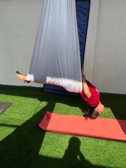 A student in a beautiful plow pose variation, fully supported by the hammock.