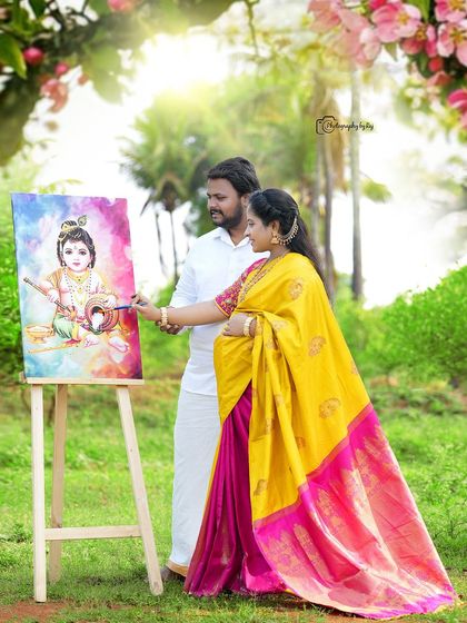 A creative outdoor portrait of a couple with a painting of Baby Krishna. The mother-to-be is wearing a vibrant yellow and pink saree.