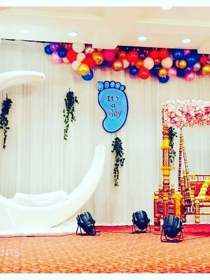 A gender reveal or baby shower theme combining a crescent moon prop with a traditional cradle. The colorful balloons and "It's a Boy/Girl" signs add to the excitement.