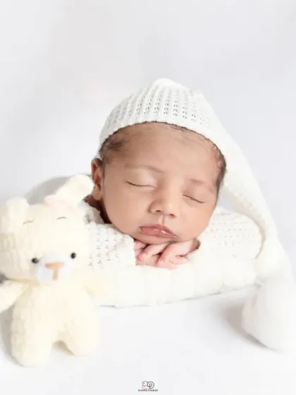 A pure and simple newborn portrait against a clean white background. The baby is dressed in a white knitted outfit and sleepy hat, showcasing their angelic features.
