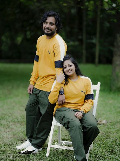 A relaxed portrait of the couple, she seated and he standing, both in matching casual wear.