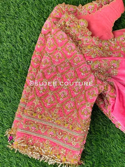 A detailed shot of the sleeve of the pink zardozi blouse. The craftsmanship is visible in the dense embroidery, featuring a mix of gold thread, pearls, and sequins, finished with delicate tassels.
