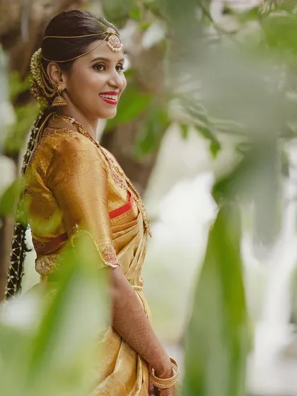 A bride in a gold Kanchipuram saree. Her custom blouse is simple yet elegant, with delicate embroidery that complements her traditional bridal look.