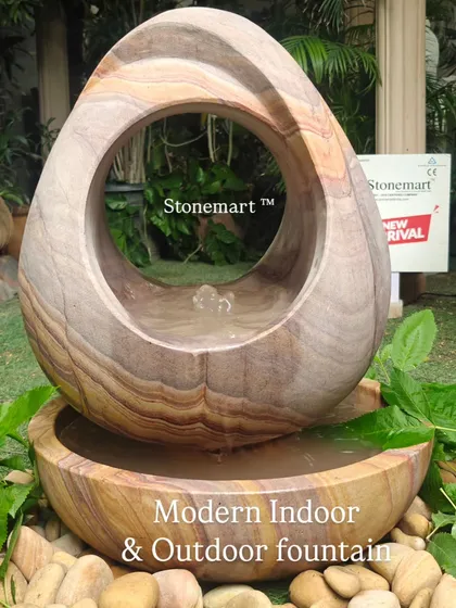 This view of the abstract Rainbow Sandstone fountain emphasizes its suitability for both indoor and outdoor settings, surrounded by natural elements.