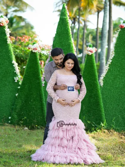 A loving couple's portrait holding a sonogram picture. The mother-to-be is wearing a pink lace gown, and they are surrounded by our unique green props.