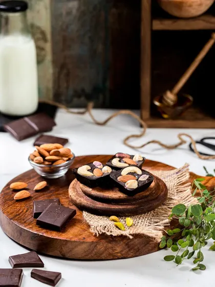 This food photography setup for artisanal chocolates uses a rustic, warm aesthetic. The arrangement with raw almonds, a bottle of milk, and wooden platters tells a story of natural ingredients and handcrafted quality.