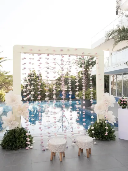 The poolside seating area, featuring a backdrop of hanging handmade organza flowers in shades of lilac and white.