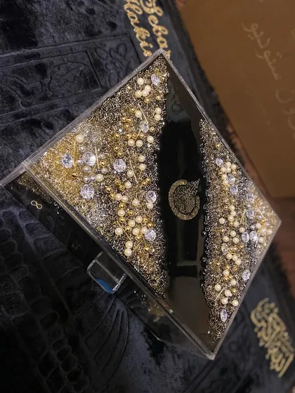 A top-down view of my trending black and gold Islamic gift set. This luxurious collection includes a personalized prayer mat, a resin Quran box, and a matching Quran holder, all heavily embellished for a grand look.