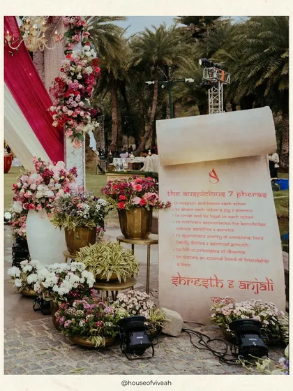 A close-up of the personalized wedding scroll, detailing the seven pheras. This element adds a deeply meaningful and narrative touch to the ceremony decor, surrounded by lush floral arrangements.