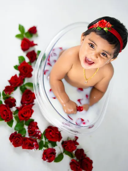 Such a happy baby enjoying her warm milk bath. The contrast of the red roses against the white milk is visually stunning.