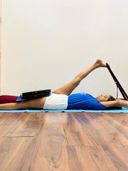 Supta Padangusthasana with weights and a belt is a therapeutic pose for the hamstrings and lower back. The weight on the thigh grounds the body, while the belt allows for a controlled stretch, making it ideal for recovery and injury prevention.