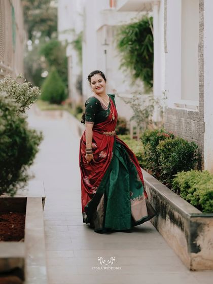 A full-length portrait of the bride in her stunning red and green half saree, looking back with a graceful smile.