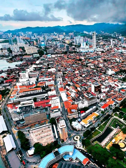 An expansive aerial photograph of George Town, Penang, showcasing the city's unique blend of colonial architecture and modern development along the coast.