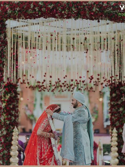 The groom places the garland around the bride's neck during the varmala ceremony. The shower of petals and the grand floral arch create a stunning backdrop for this key ritual.