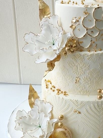 A close-up of the three-tier anniversary cake for a jeweler, showing the intricate textures and the delicate, handcrafted sugar flowers with gold-painted edges.