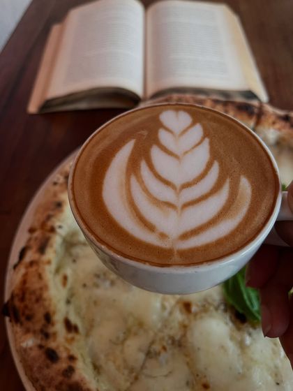 A perfect cup of coffee with beautiful latte art, a good book, and a pizza. What more could you need?