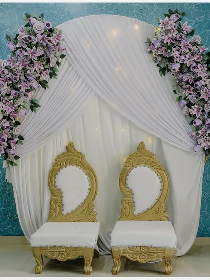 The elegant and simple decor for the engagement ceremony, featuring a white draped backdrop with floral accents and ornate chairs.