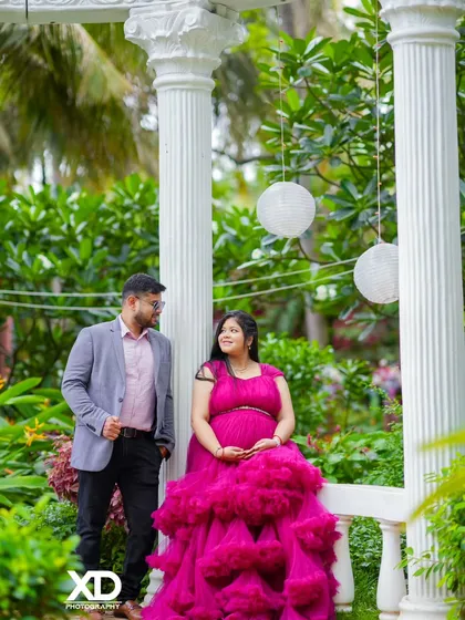 A relaxed couple's portrait in a garden, with the mother-to-be seated on an elegant white bench.