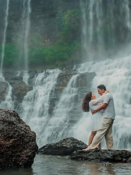 A dramatic and romantic pose in front of a waterfall. The groom lifts the bride, creating a powerful silhouette against the rushing water and rocks.