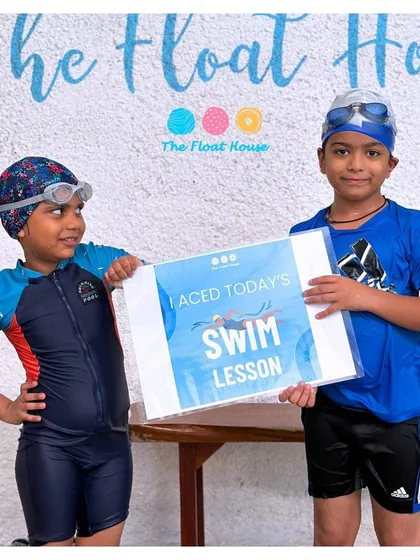 Two swim buddies proudly show off their 'I Aced Today's Swim Lesson' sign. Learning is always more fun with a friend by your side.