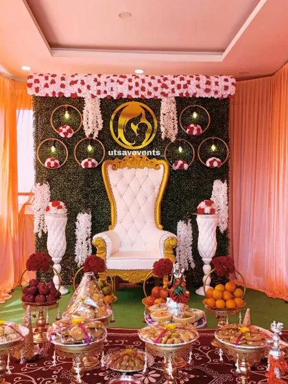 A lovely baby shower setup with a greenery wall, a white throne, and hanging floral decor. The room is draped in peach curtains to match the elegant theme.