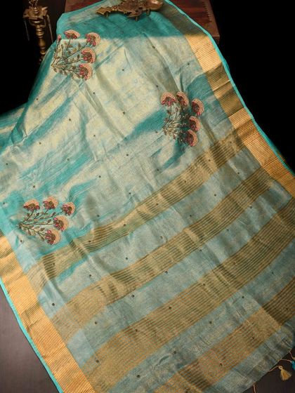A beautiful turquoise linen saree with floral embroidery and a subtle gold border. This piece is fresh, elegant, and perfect for a sunny day.