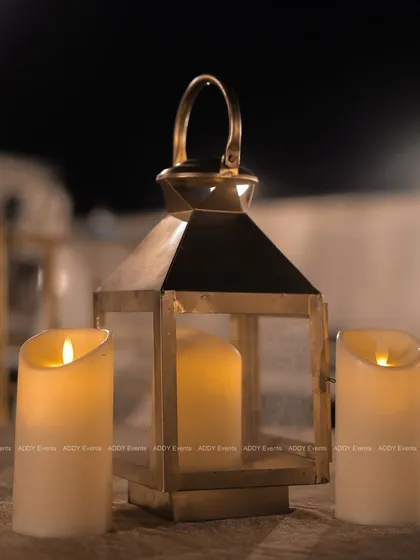 A close-up of a rustic brass lantern and flameless candles. This small detail adds a warm, intimate glow to tables or lounge areas, showcasing our attention to creating the right mood.