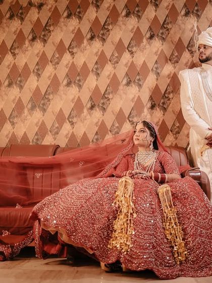 A formal portrait of the couple in their wedding outfits, with the groom standing behind the seated bride.
