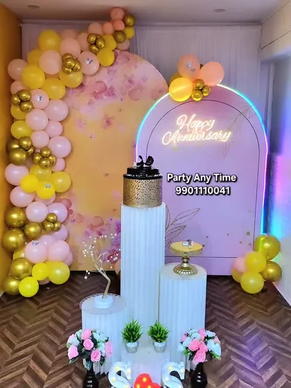 Celebrate your special milestones with a custom anniversary decoration. This setup uses a soft color palette with yellow and pink balloons, a floral backdrop, and a "Happy Anniversary" neon sign to create a romantic atmosphere.