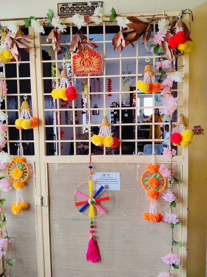 This is a door decoration for a festive occasion, using a variety of colorful handmade hangings and artificial flowers to create a welcoming and cheerful entrance.