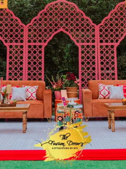 The main seating lounge for the Mehendi, featuring comfortable sofas against a backdrop of pink jaali screens. The space is decorated with colourful cushions and unique centerpieces.