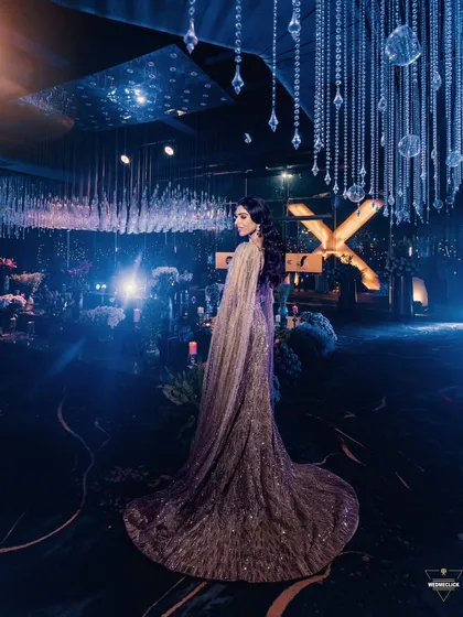 A breathtaking wide shot of the bride in a glamorous gown, standing in a lavishly decorated reception hall with a celestial theme.
