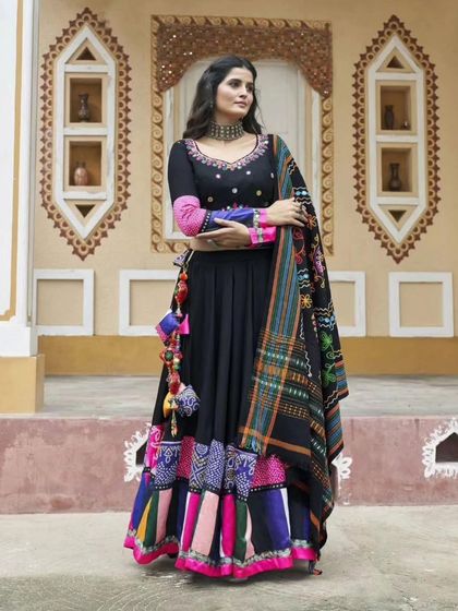 A model showcasing a vibrant and colorful outfit perfect for Navratri. The black base with multi-color embroidery and mirror work is ideal for Garba nights.