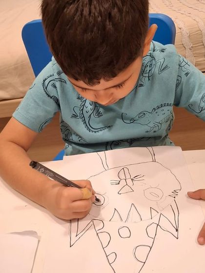 A young student carefully outlines a cat with a party hat. This is the first step in our process, where we focus on getting the basic drawing down before adding color.