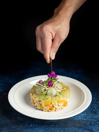 A gourmet plated dish, showing the final touch being added by the chef. This kind of shot emphasizes precision, artistry, and the fine-dining experience.