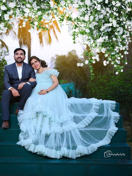 A beautiful couple's portrait on green steps, surrounded by white blossoms. The mother-to-be's light blue ruffled gown creates a serene and elegant look.