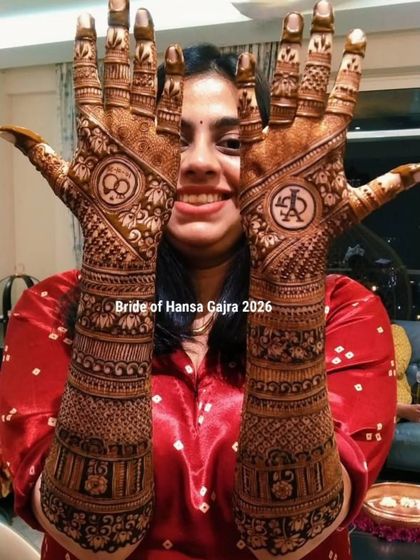 A happy bride showing off her engagement mehendi. The back of her hands features personalized initials and infinity symbols, surrounded by intricate traditional bands.