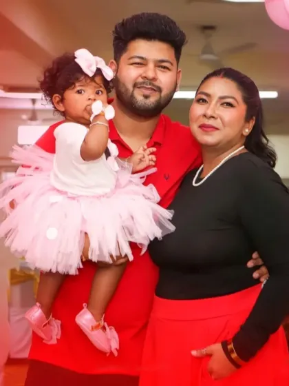 A lovely family portrait taken at a first birthday party. The parents and their little girl are dressed in coordinated colors, matching the festive party atmosphere.