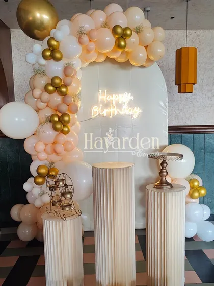A beautiful pastel and gold balloon arrangement on a white arched backdrop with a neon sign.
